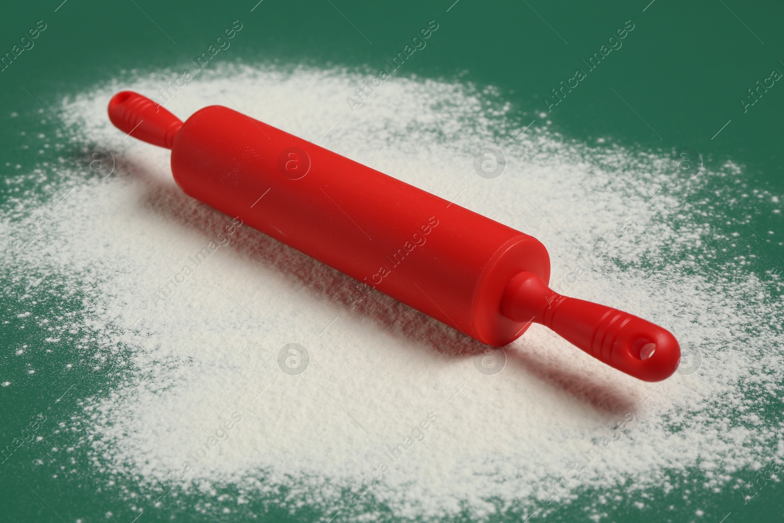 Photo of Red rolling pin and flour on green background