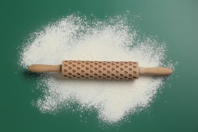 Photo of Wooden rolling pin and flour on green background, top view