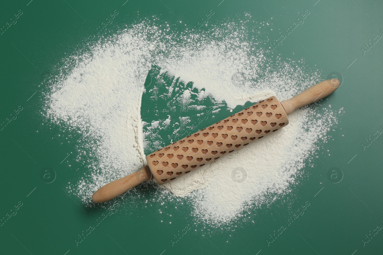 Photo of Wooden rolling pin and flour on green background, top view