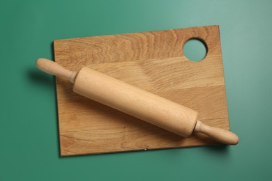 Photo of Rolling pin and wooden board on green background, top view