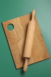 Photo of Rolling pin and wooden board on green background, top view