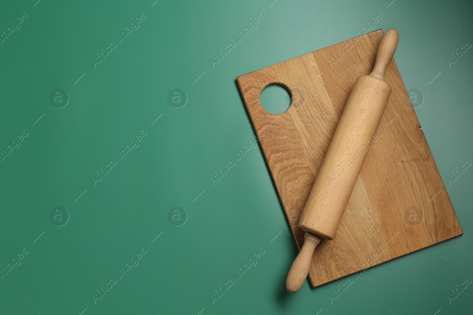 Photo of Rolling pin and wooden board on green background, top view. Space for text