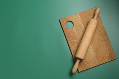 Photo of Rolling pin and wooden board on green background, top view. Space for text