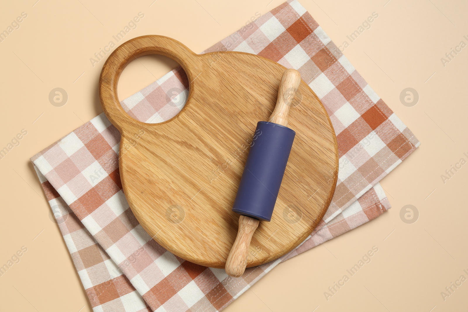 Photo of Rolling pin, wooden board and checkered napkin on beige background, top view