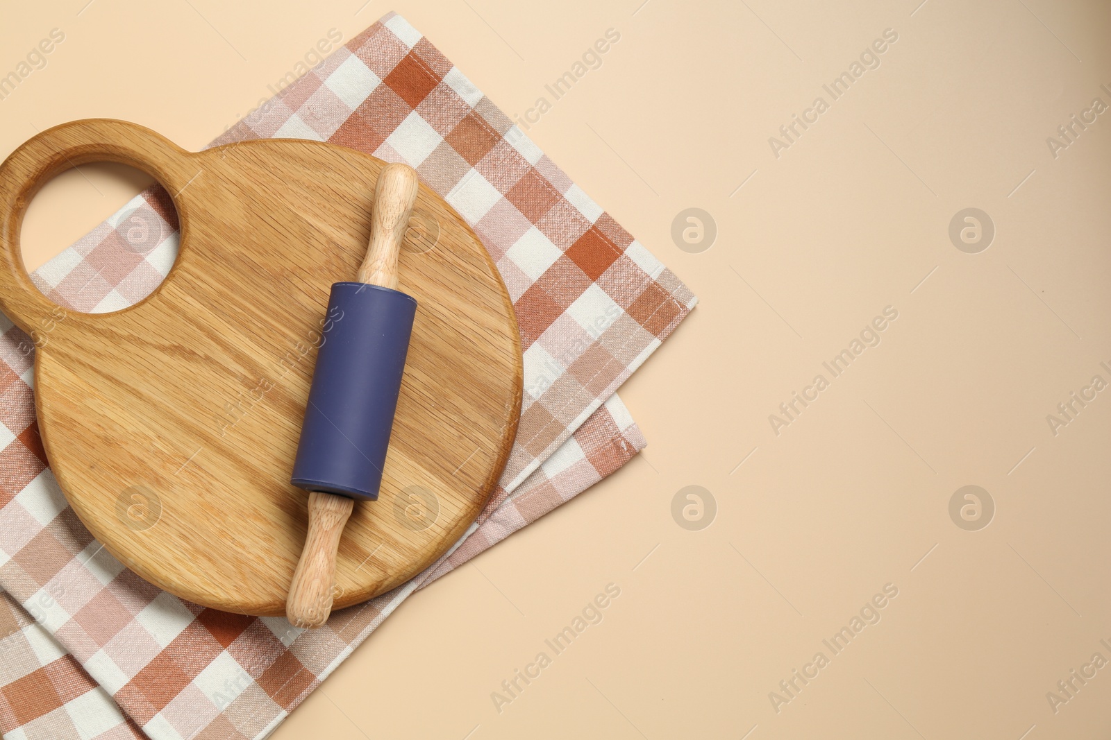 Photo of Rolling pin, wooden board and checkered napkin on beige background, top view. Space for text