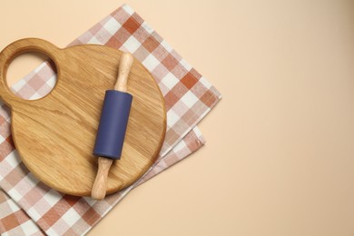 Photo of Rolling pin, wooden board and checkered napkin on beige background, top view. Space for text