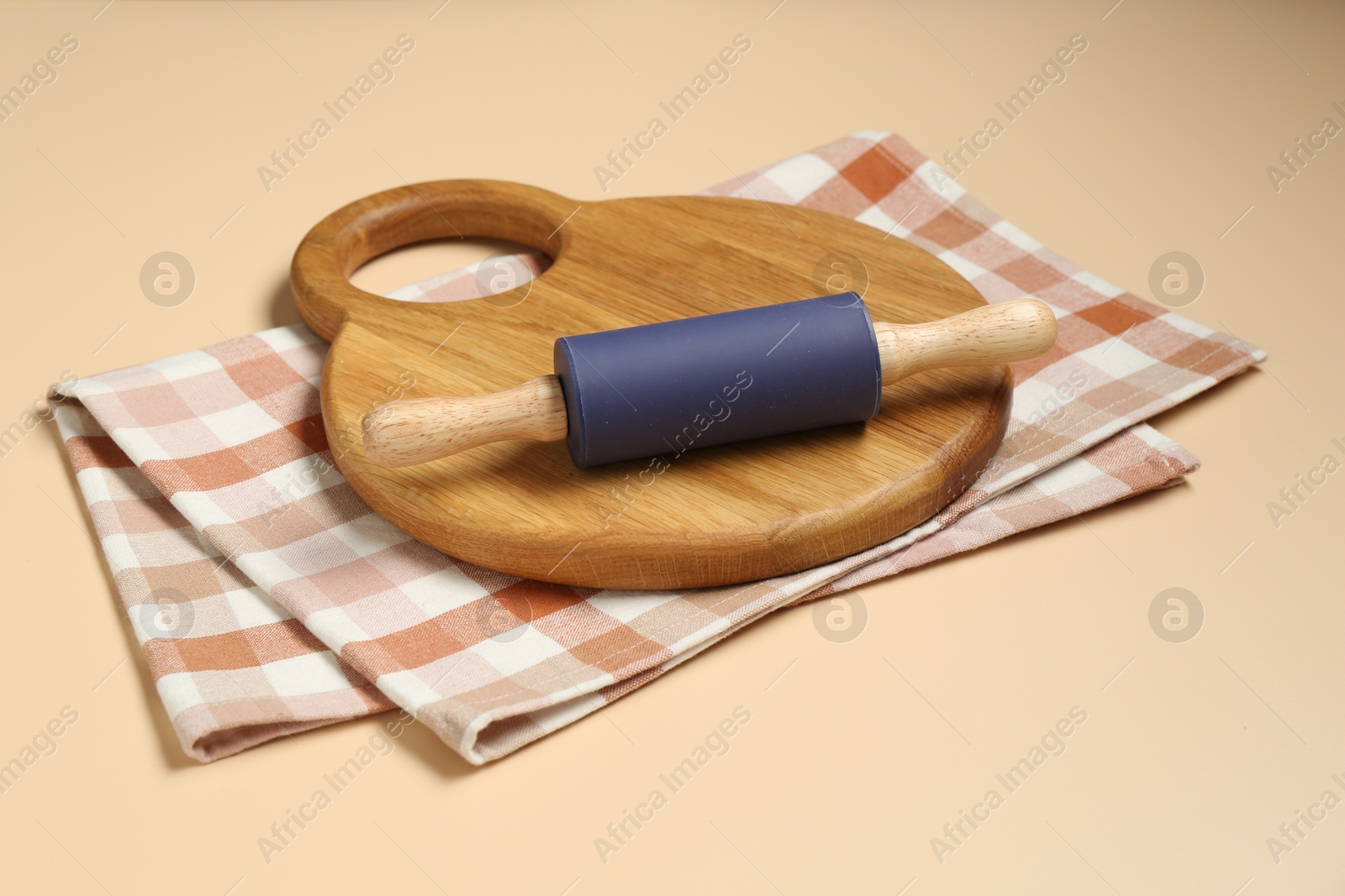 Photo of Rolling pin, wooden board and checkered napkin on beige background