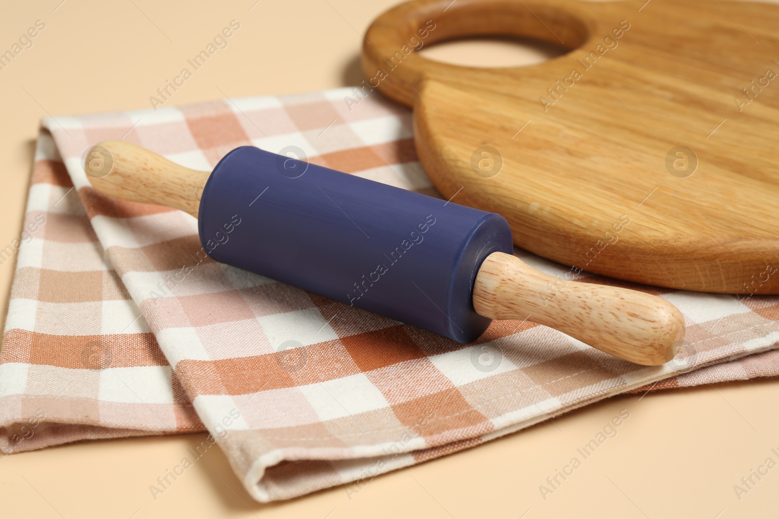 Photo of Rolling pin, wooden board and checkered napkin on beige background, closeup