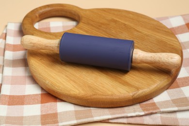 Photo of Rolling pin, wooden board and checkered napkin on beige background, closeup