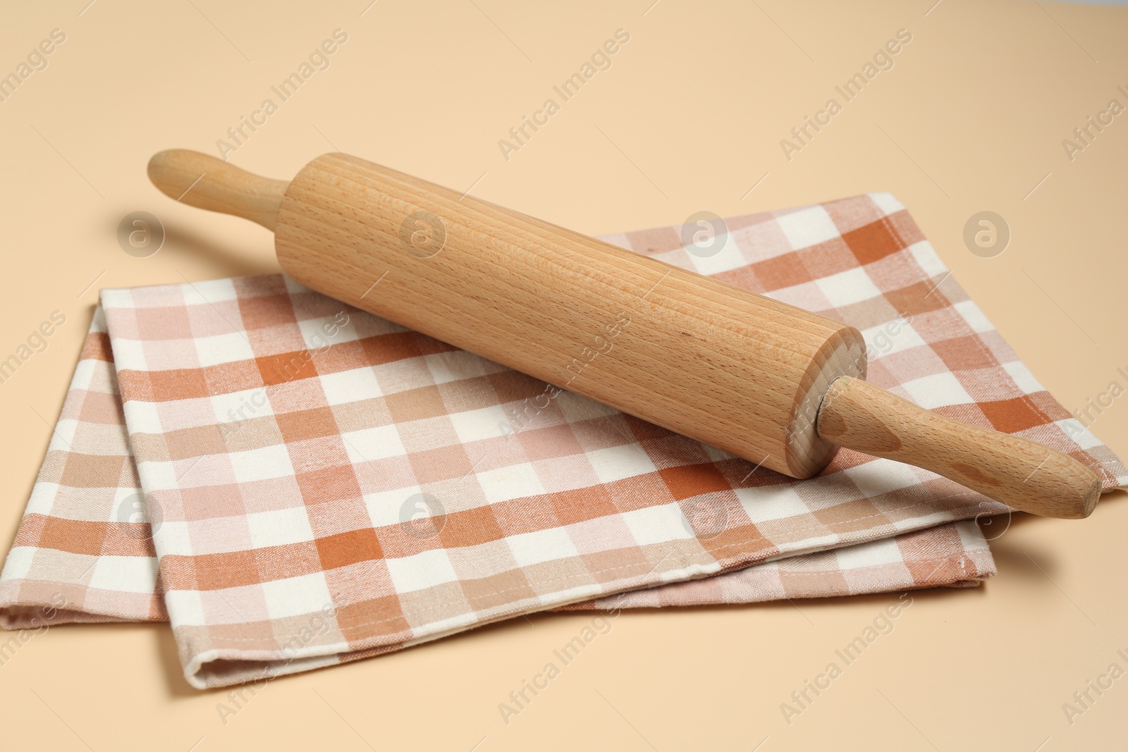 Photo of Wooden rolling pin and checkered napkin on beige background