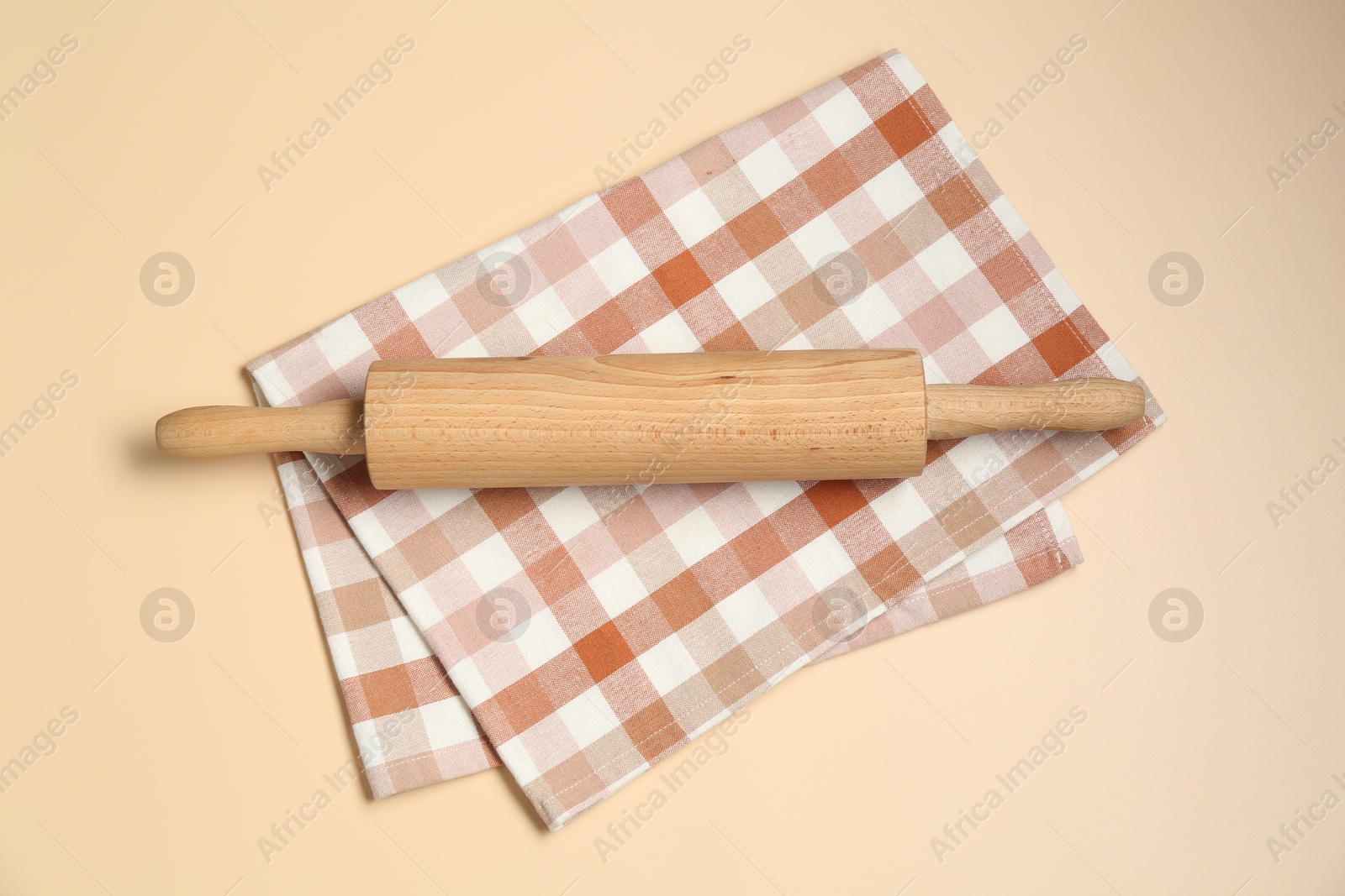 Photo of Wooden rolling pin and checkered napkin on beige background, top view