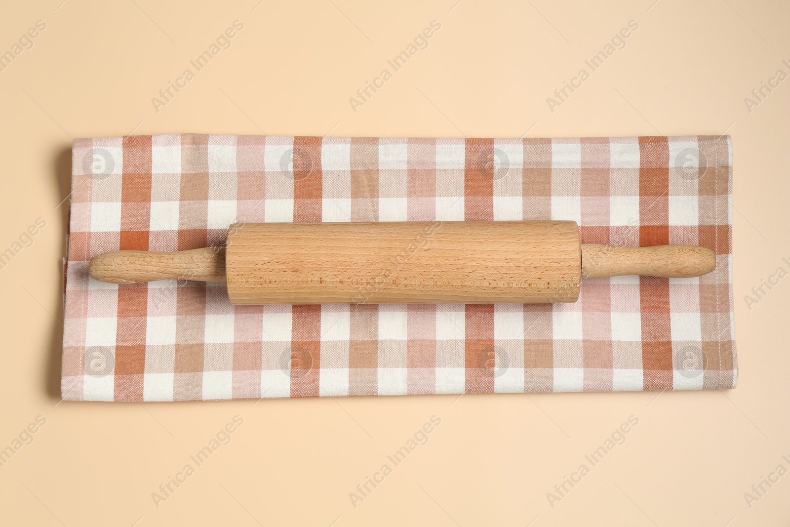 Photo of Wooden rolling pin and checkered napkin on beige background, top view