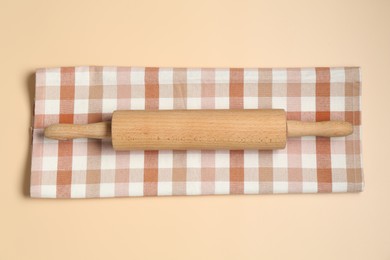 Photo of Wooden rolling pin and checkered napkin on beige background, top view