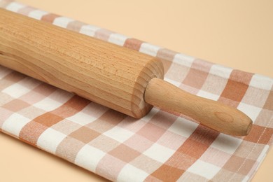 Photo of Wooden rolling pin and checkered napkin on beige background, closeup