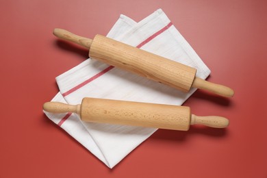 Photo of Wooden rolling pins and napkin on red background, flat lay