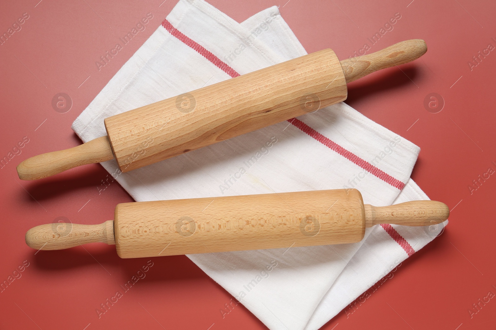 Photo of Wooden rolling pins and napkin on red background, flat lay