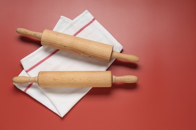 Photo of Wooden rolling pins and napkin on red background, flat lay