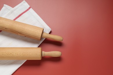 Photo of Wooden rolling pins and napkin on red background, flat lay. Space for text