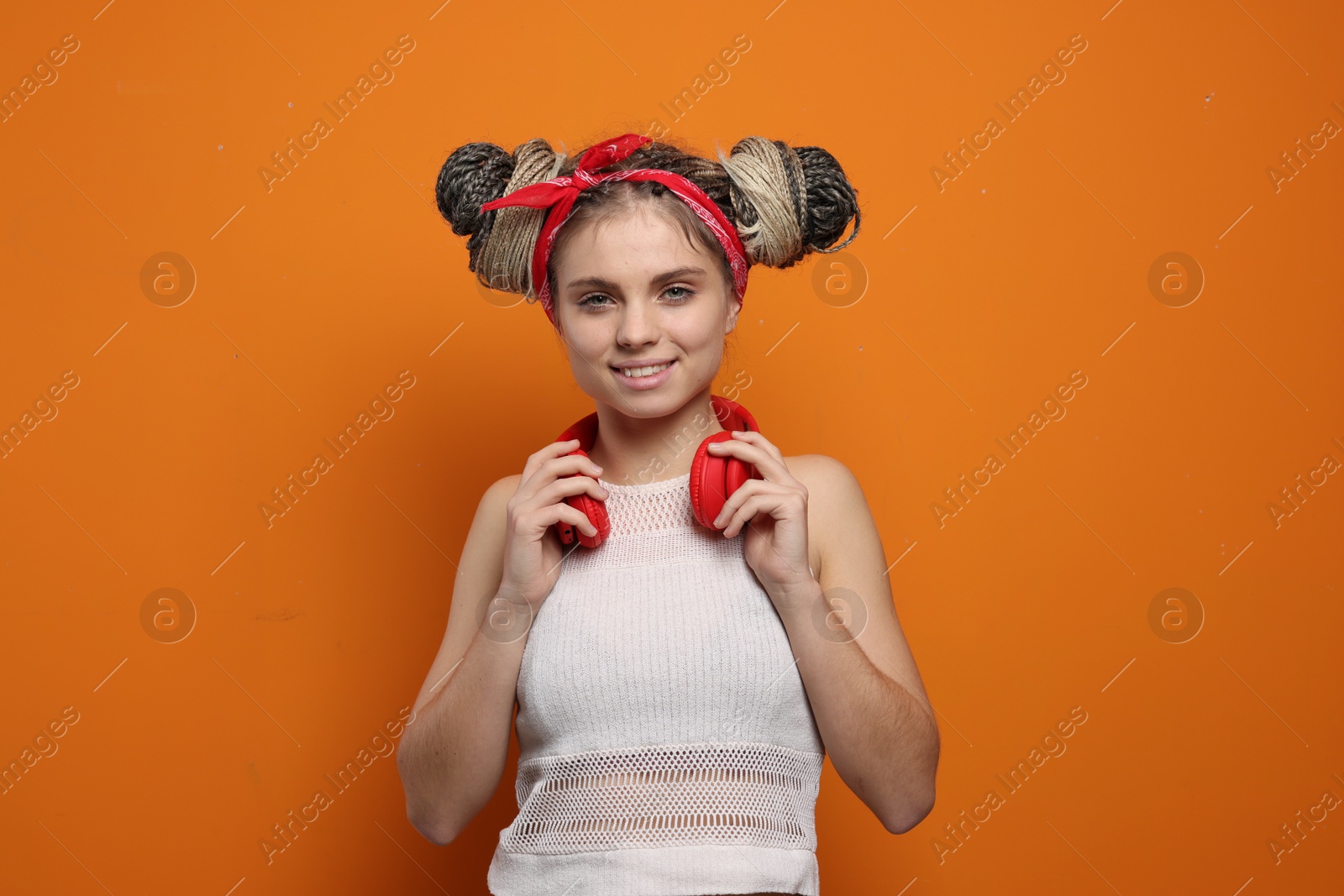 Photo of Beautiful woman with braided double buns and headphones on orange background