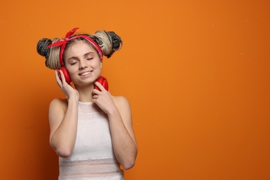 Photo of Beautiful woman with braided double buns and headphones on orange background, space for text