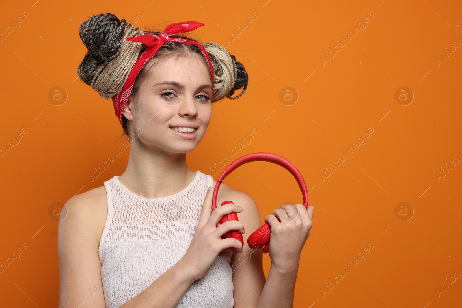 Photo of Beautiful woman with braided double buns and headphones on orange background, space for text