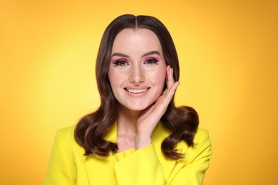 Photo of Portrait of beautiful young woman with stylish makeup and gorgeous hair on yellow background