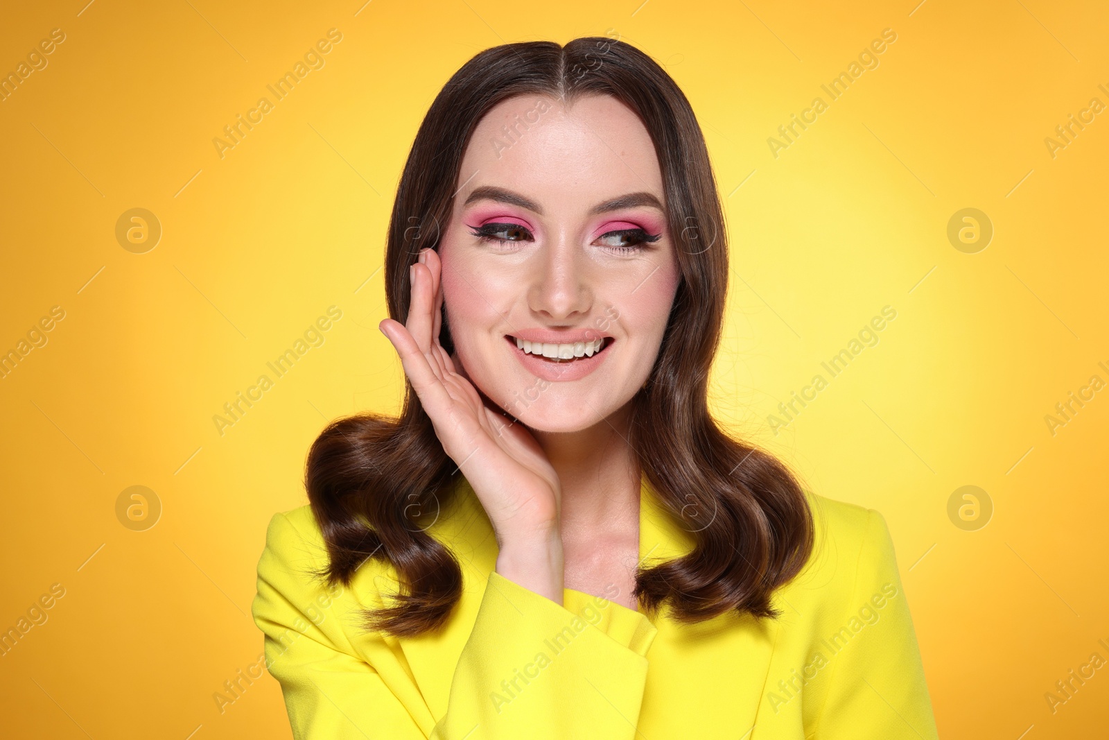 Photo of Portrait of beautiful young woman with stylish makeup and gorgeous hair on yellow background