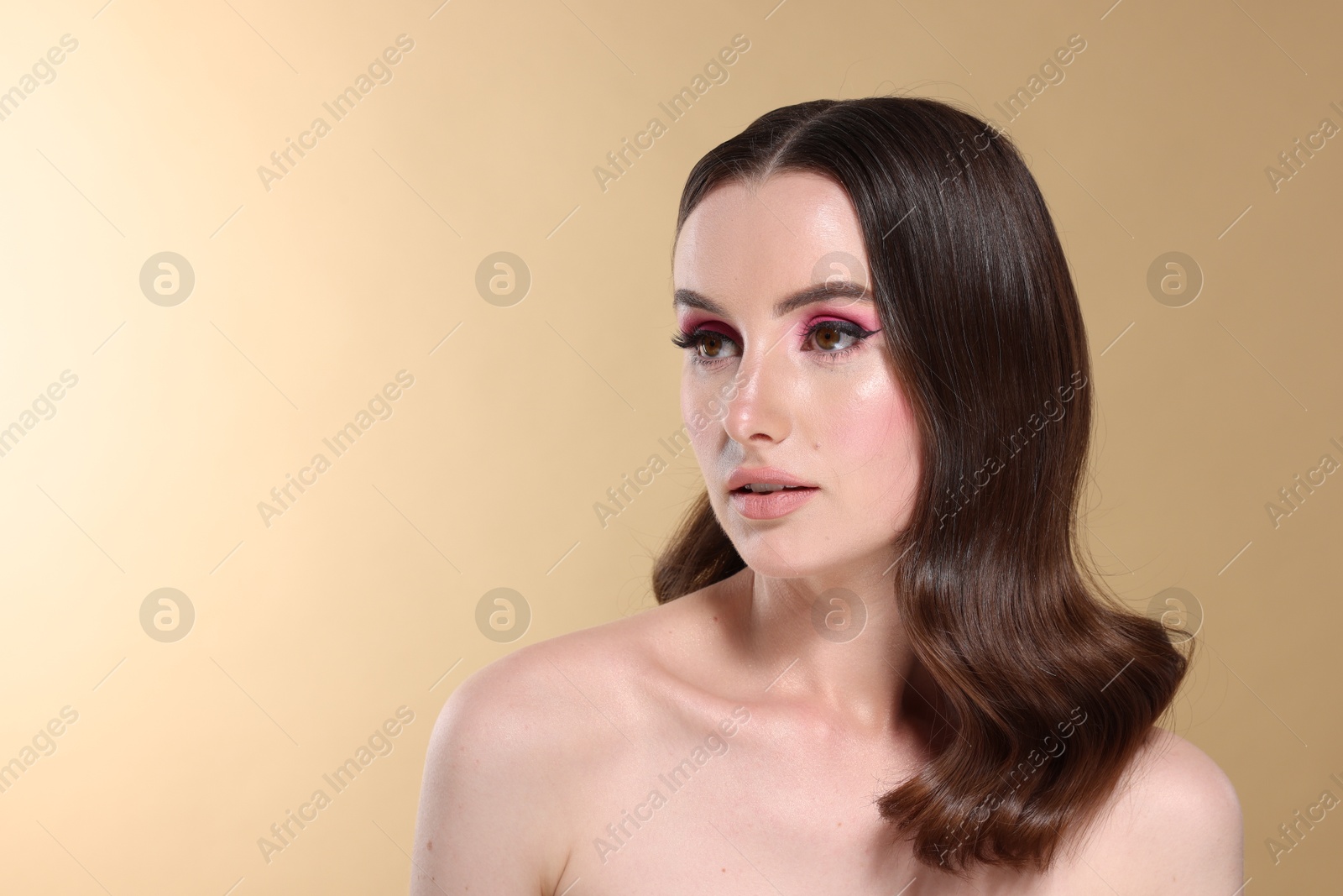 Photo of Portrait of beautiful young woman with stylish makeup and gorgeous hair on beige background. Space for text