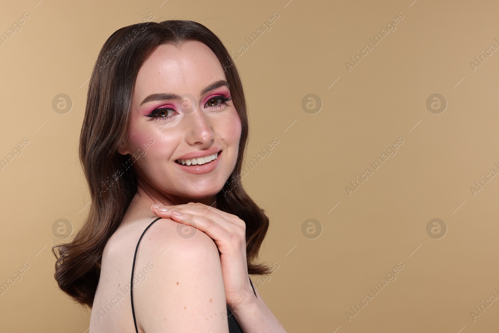 Photo of Portrait of beautiful young woman with stylish makeup and gorgeous hair on beige background. Space for text