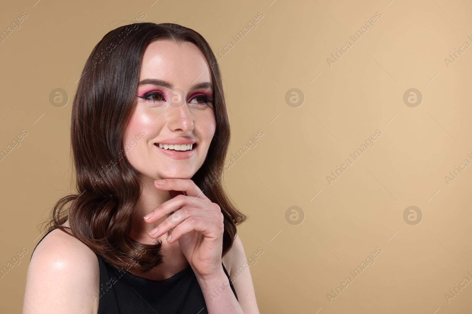 Photo of Portrait of beautiful young woman with stylish makeup and gorgeous hair on beige background. Space for text