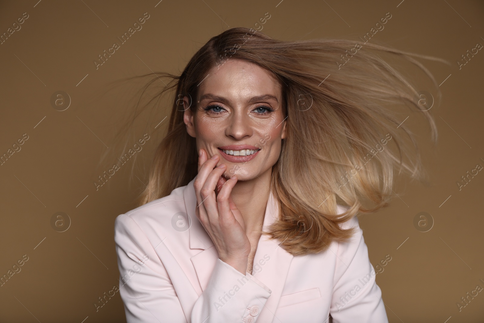 Photo of Portrait of beautiful happy woman with straight blonde hair on light brown background