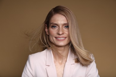 Photo of Portrait of beautiful happy woman with straight blonde hair on light brown background