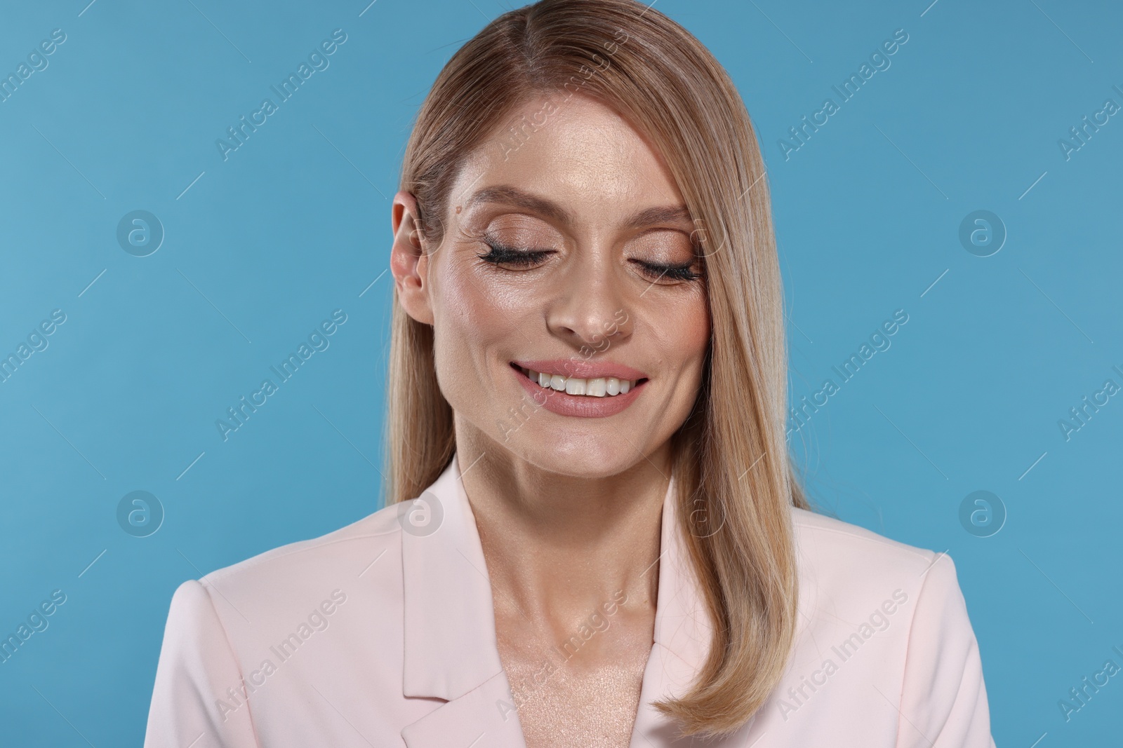 Photo of Portrait of beautiful happy woman with straight blonde hair and makeup on light blue background