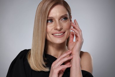 Photo of Portrait of beautiful happy woman with straight blonde hair on grey background