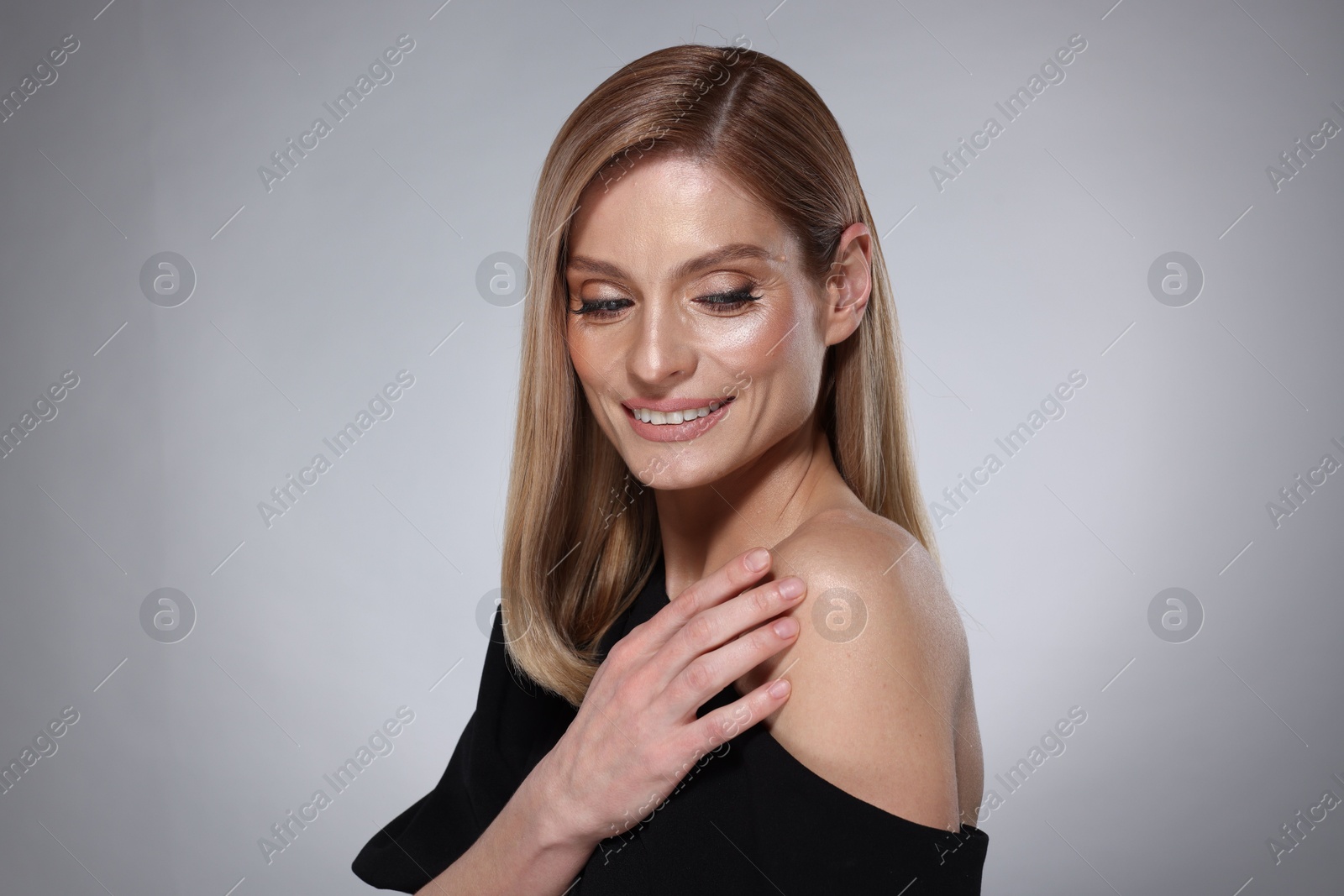 Photo of Portrait of beautiful happy woman with straight blonde hair and stylish makeup on grey background