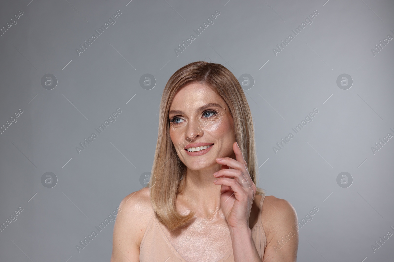 Photo of Portrait of beautiful happy woman with straight blonde hair on grey background