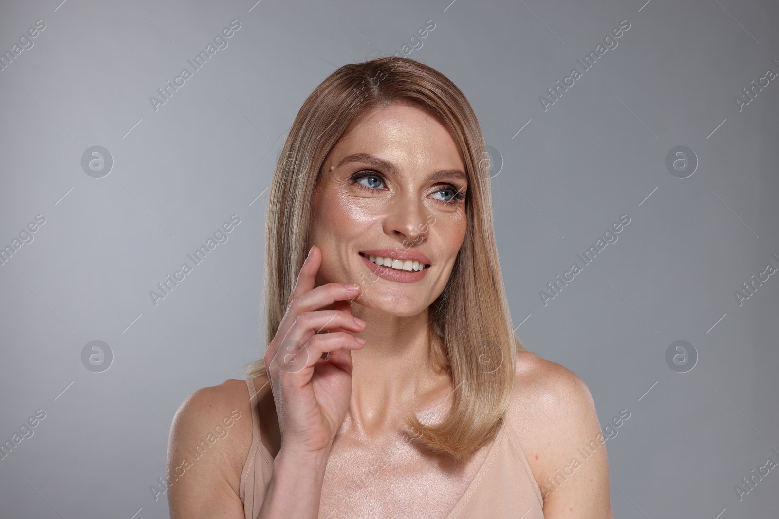 Photo of Portrait of beautiful happy woman with straight blonde hair on grey background