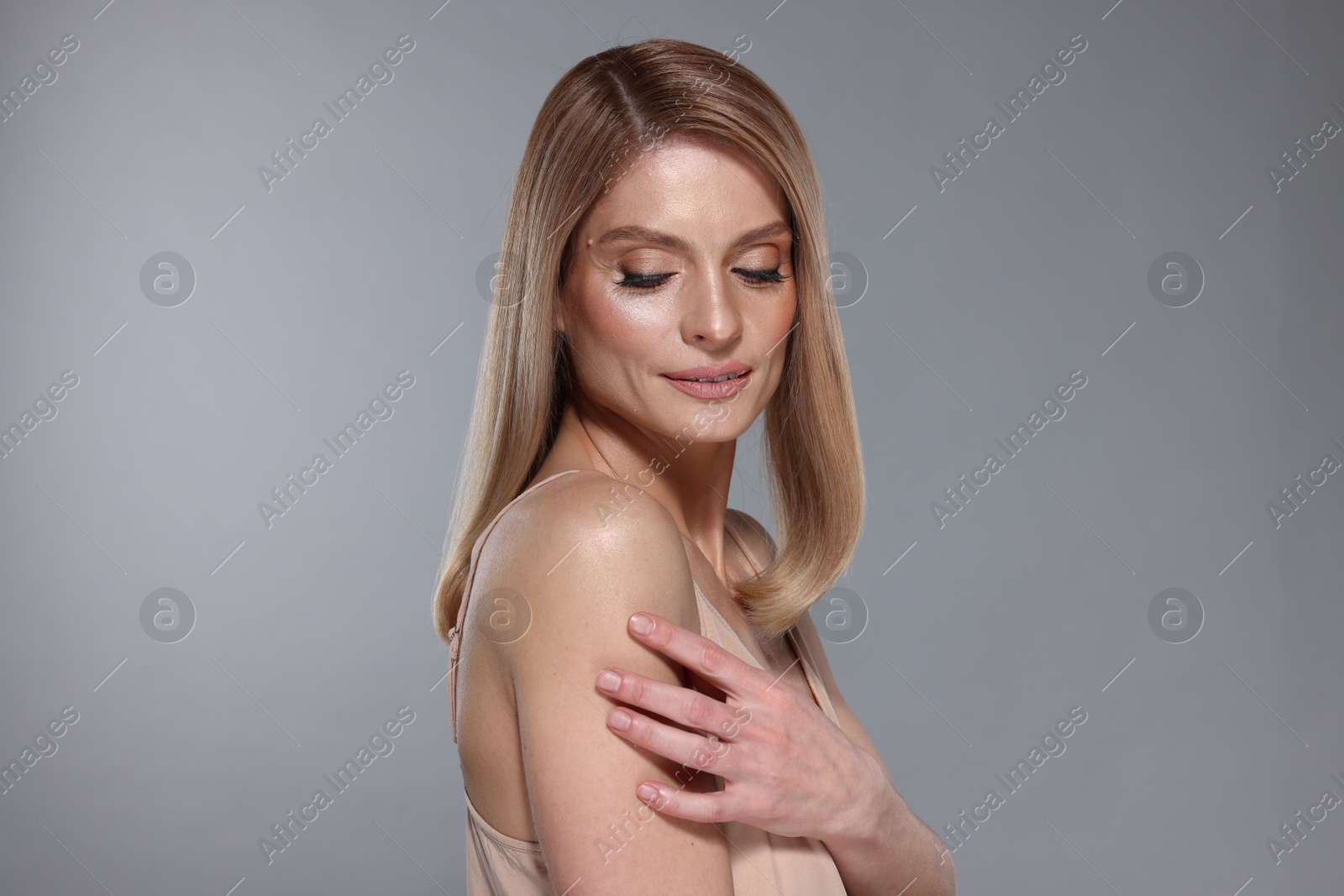 Photo of Portrait of beautiful woman with straight blonde hair and stylish makeup on grey background