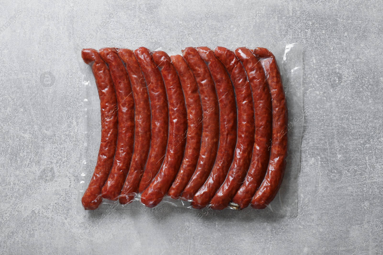 Photo of Pack of dry smoked sausages on grey table, top view