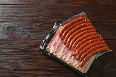 Photo of Packs of dry smoked sausages and sliced bacon on wooden table, top view. Space for text