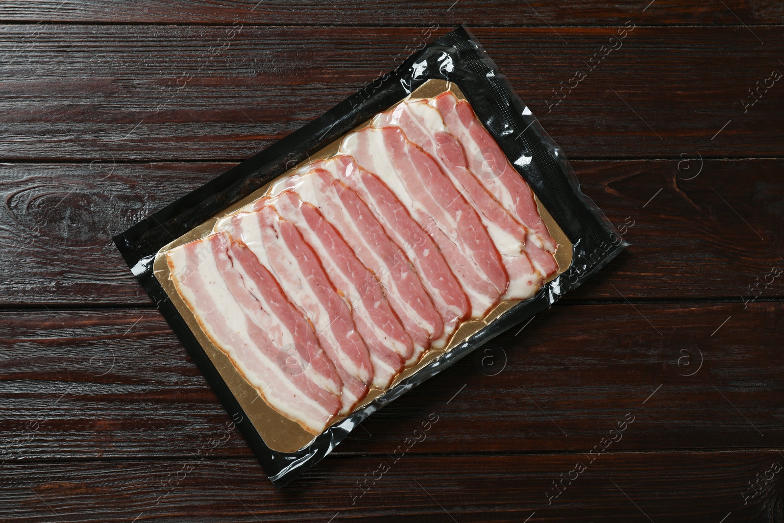 Photo of Pack of sliced bacon on wooden table, top view