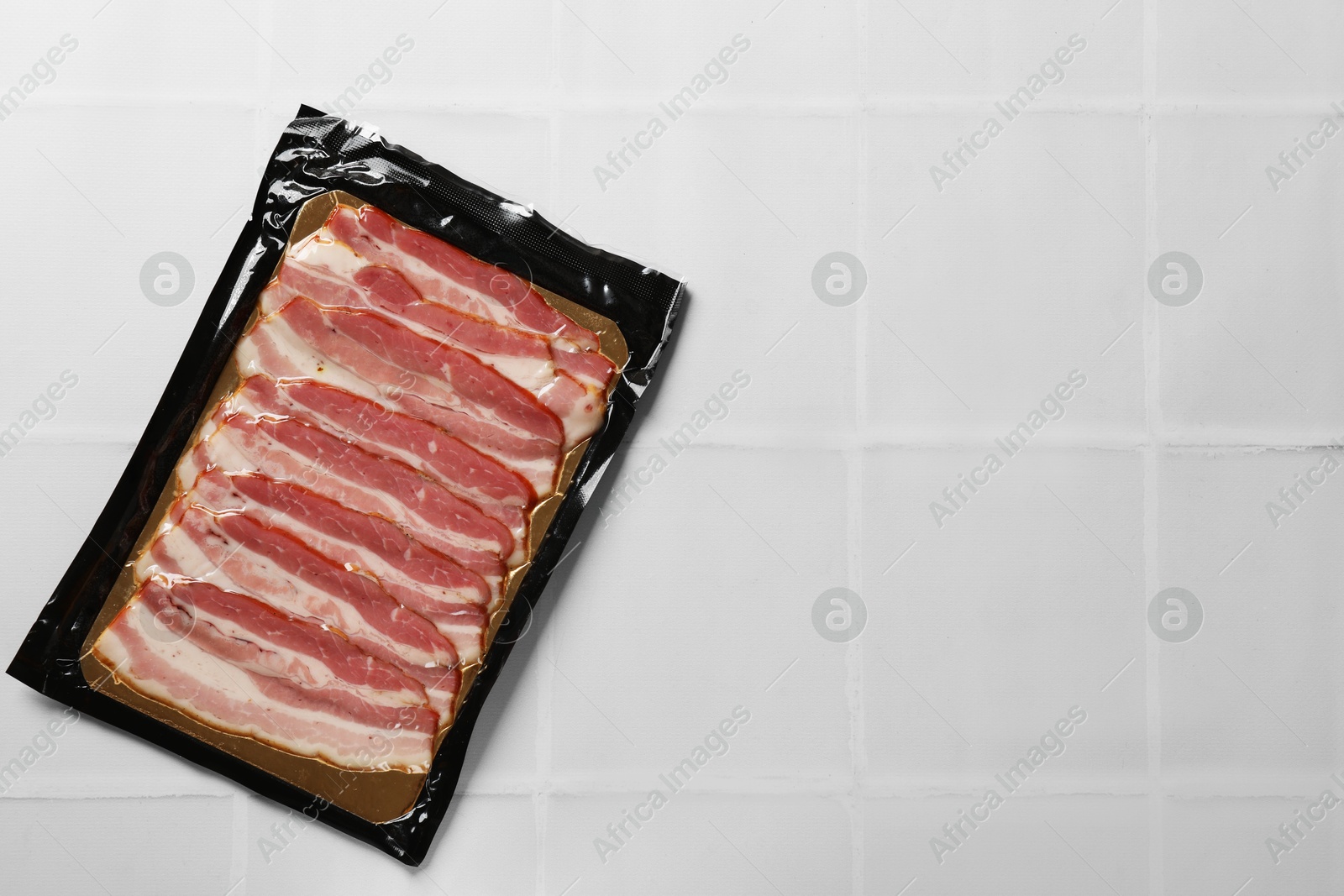 Photo of Pack of sliced bacon on white tiled table, top view. Space for text