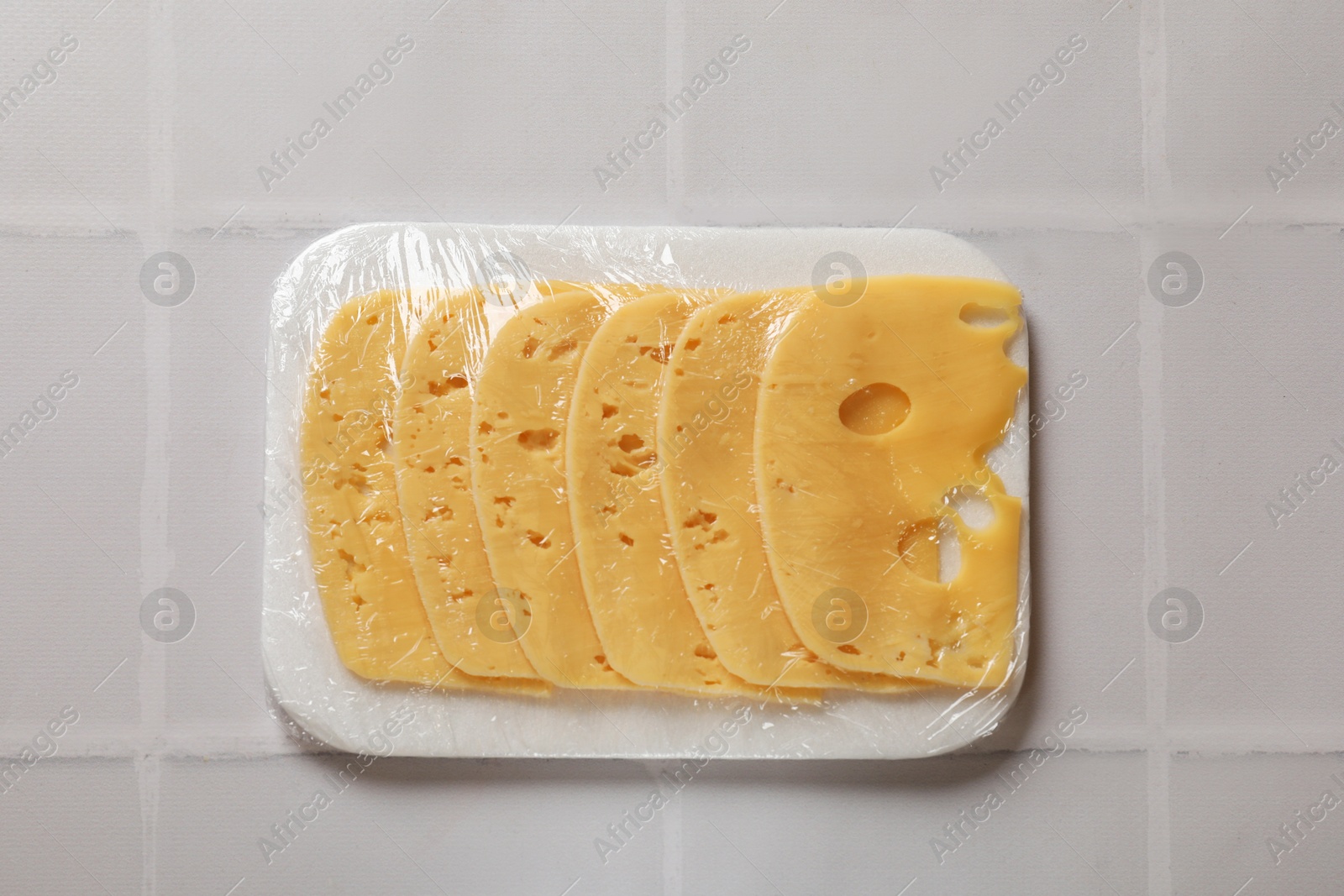 Photo of Pack of sliced cheese on white tiled table, top view