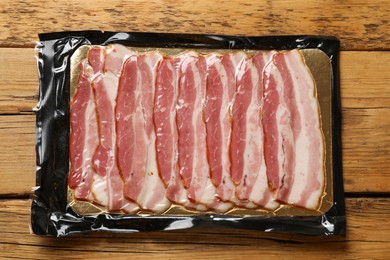 Photo of Pack of sliced bacon on wooden table, top view