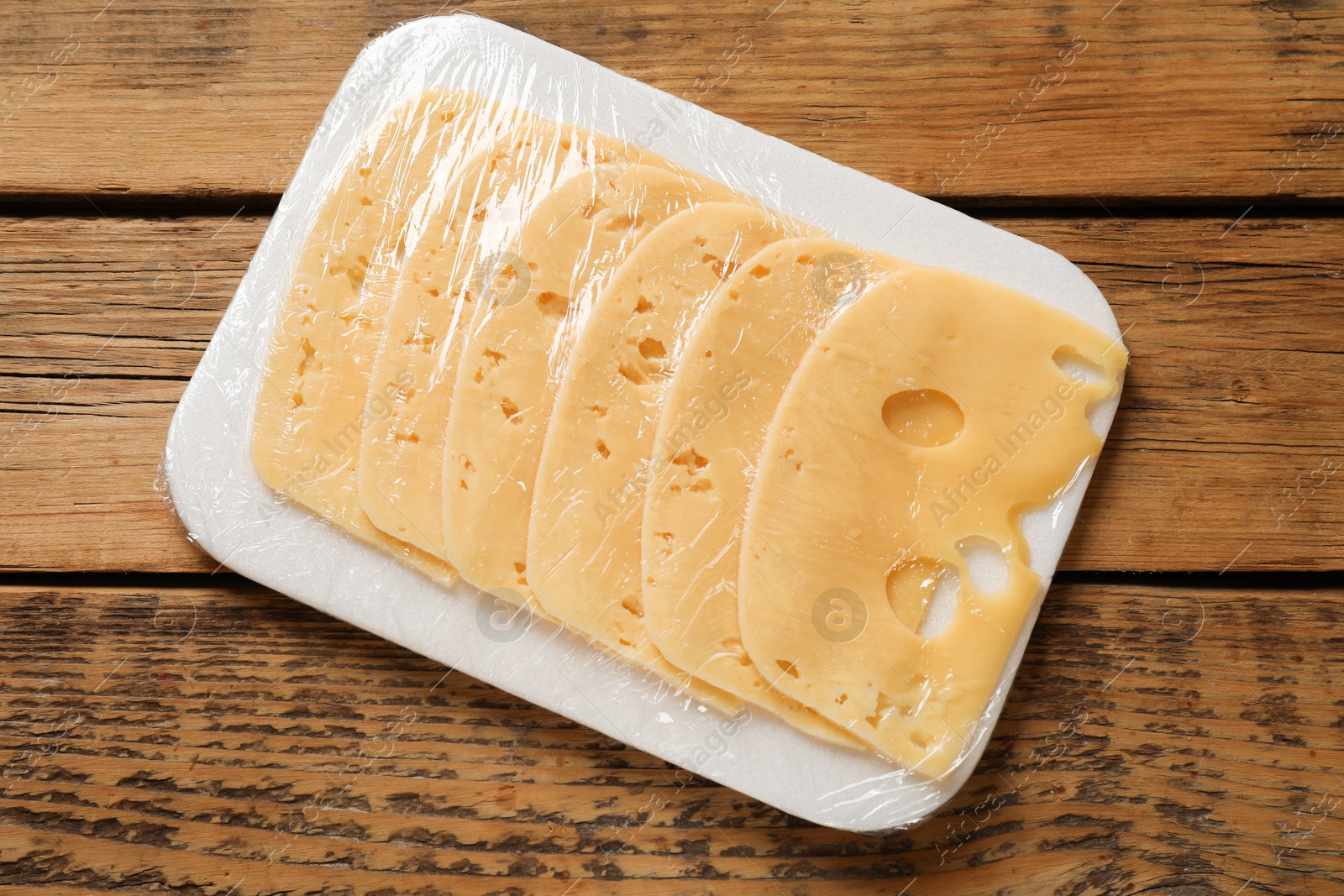 Photo of Pack of sliced cheese on wooden table, top view