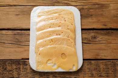 Photo of Pack of sliced cheese on wooden table, top view