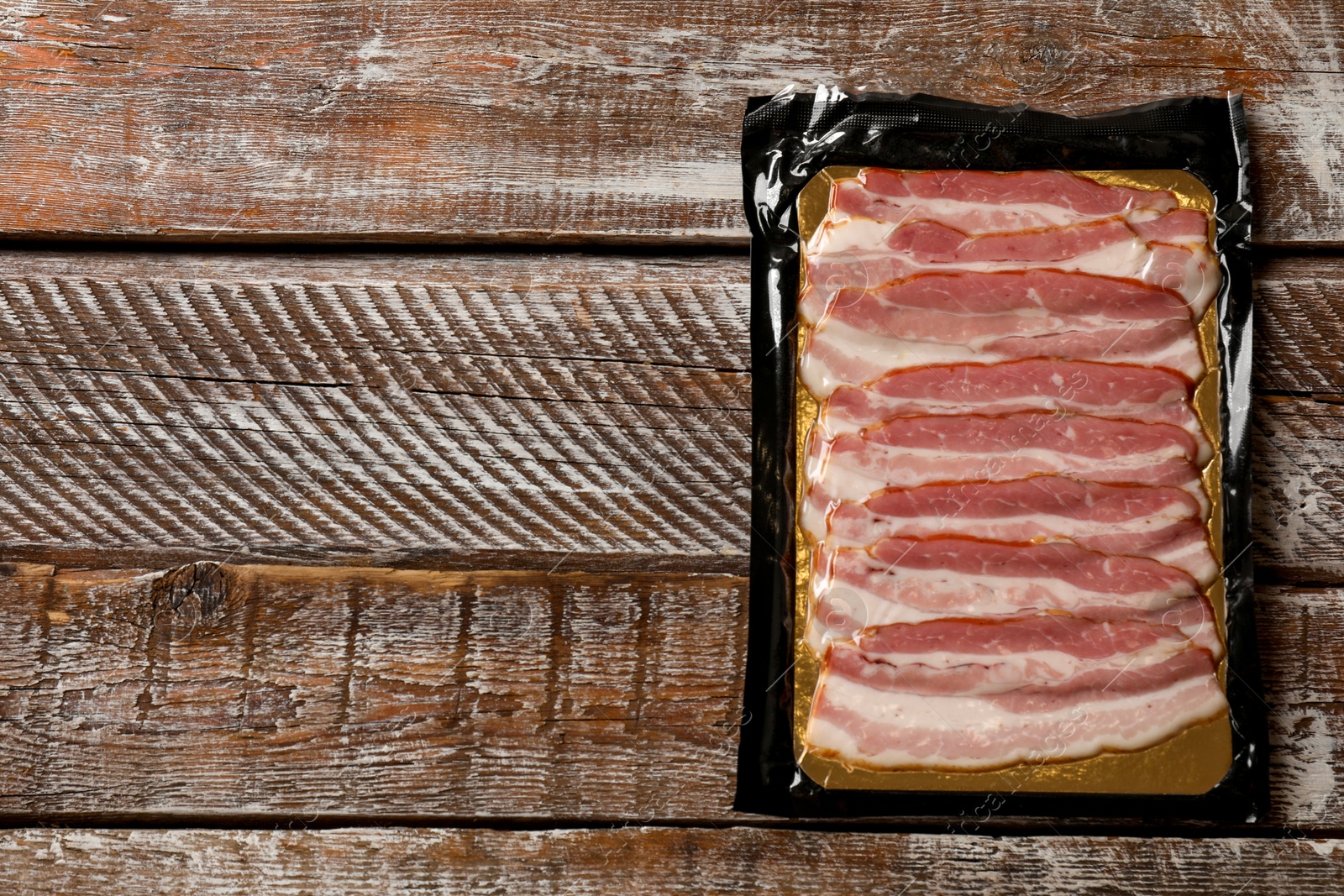 Photo of Pack of sliced bacon on wooden table, top view. Space for text