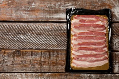 Photo of Pack of sliced bacon on wooden table, top view. Space for text