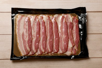 Photo of Pack of sliced bacon on wooden table, top view