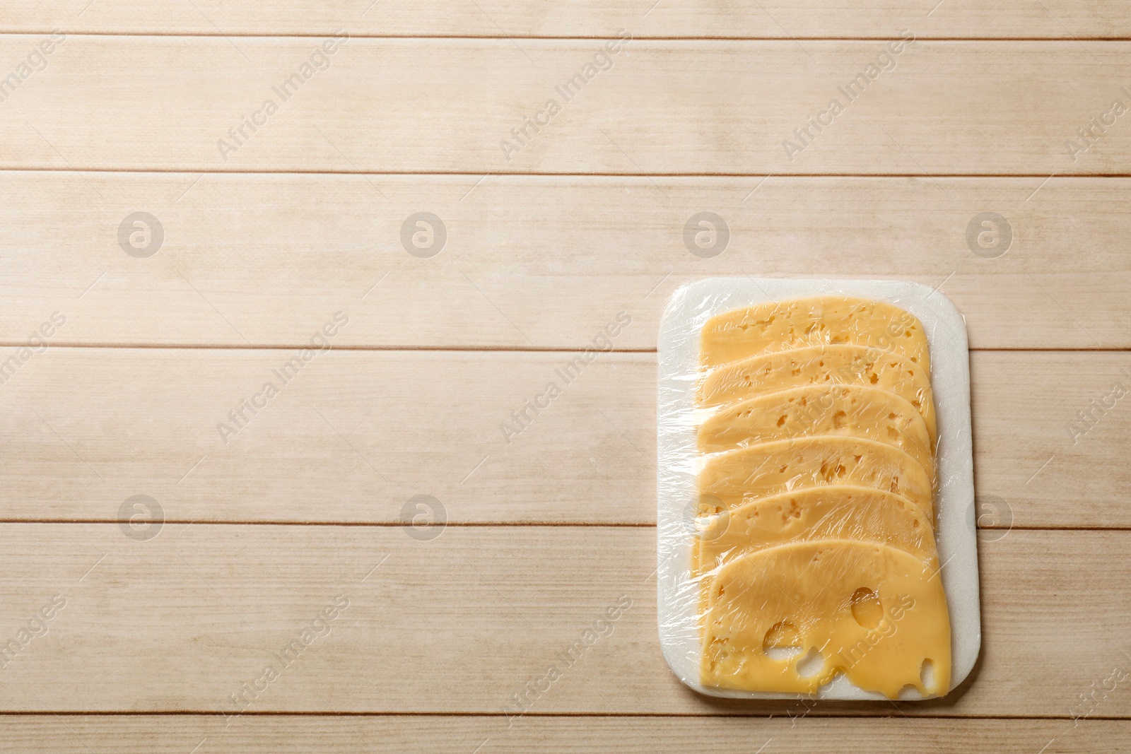 Photo of Pack of sliced cheese on wooden table, top view. Space for text